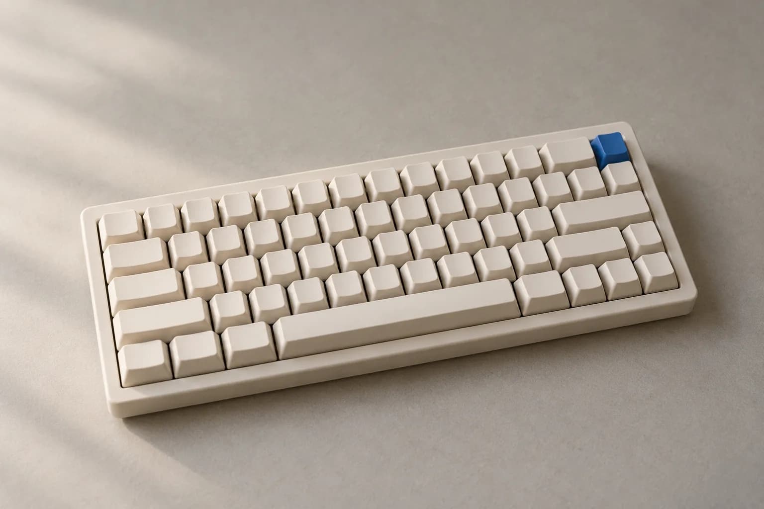 A low mechanical keyboard on warm grey paper with every keycap off-white except one electric-blue key, blank keycaps with no legends, in soft window light.
