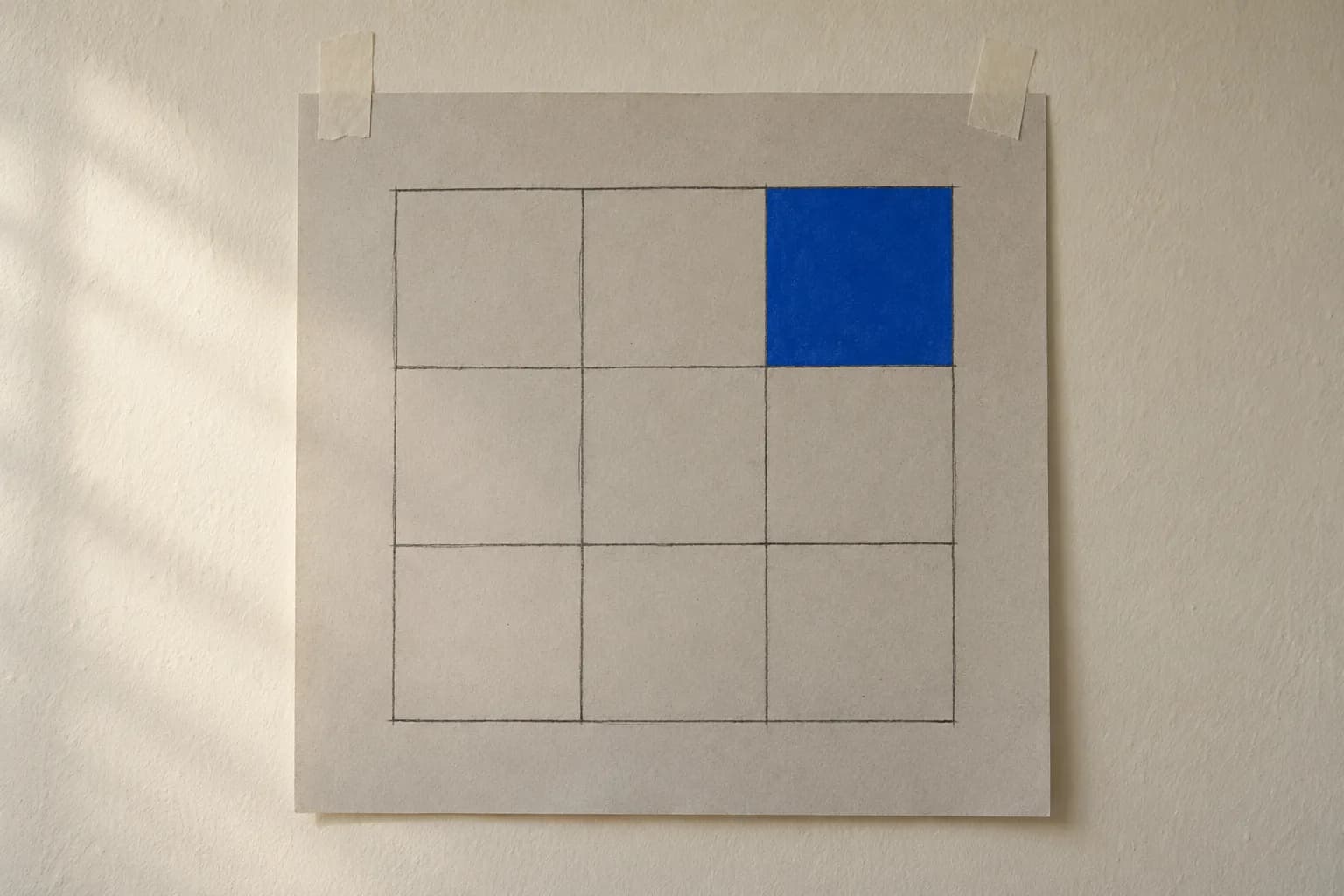 A hand-drawn calendar grid of nine empty squares on a large sheet of paper pinned to a wall with electric-blue tape, one square filled with a solid blue block.